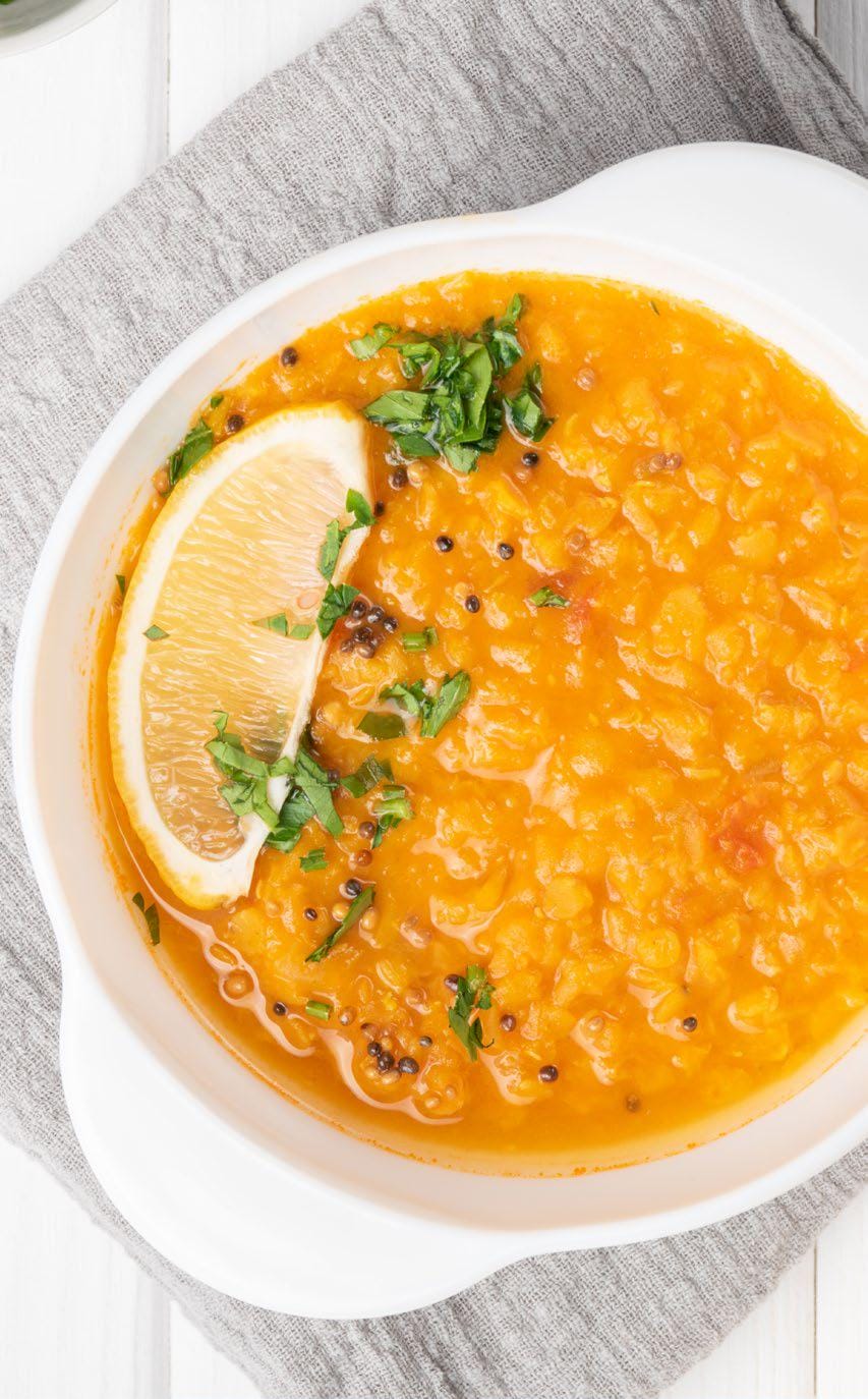 Bowl of creamy lentil soup garnished with fresh herbs and a lemon wedge, served on a light linen cloth.