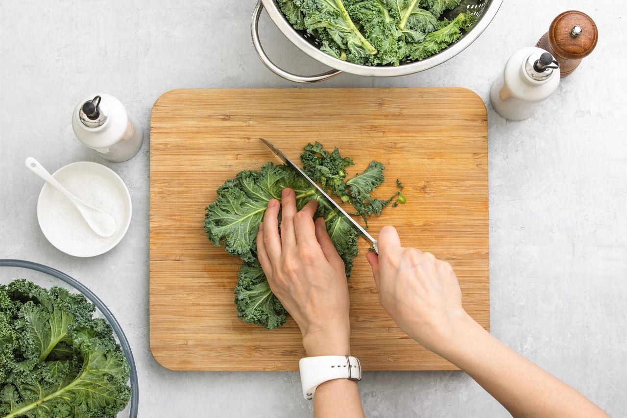 Overhead view of a person slicing a kale leaf.