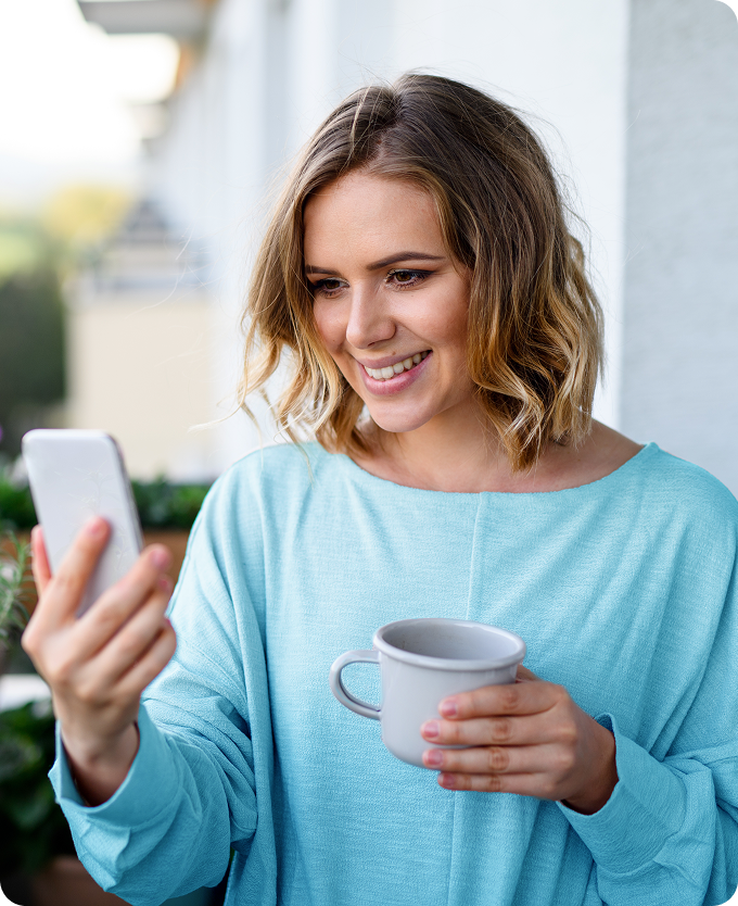 A young woman holds a cup of coffee and is speaking to a healthcare provider with her phone.