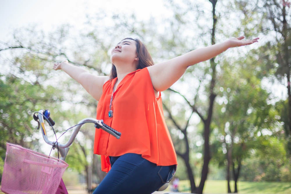 Happy asian woman with outstretched arms riding a bicycle outdoors in a park