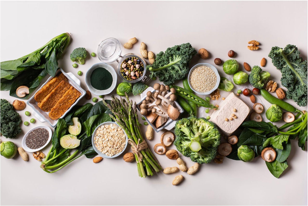 Overhead view of a table with a spread of various vegetables, plant-based proteins and nuts.