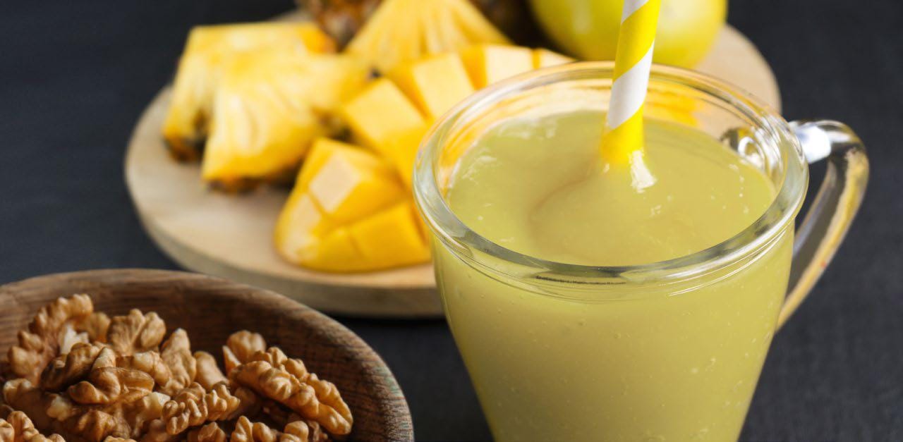Smoothie in a glass with a straw, bowl of pecans, and plate of pineapple in the background