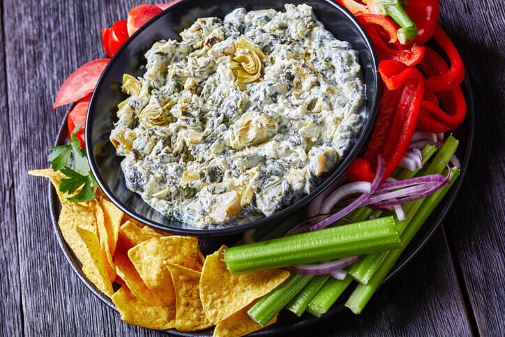 Bowl of spinach artichoke dip surrounded by chips and cut vegetables for dipping.