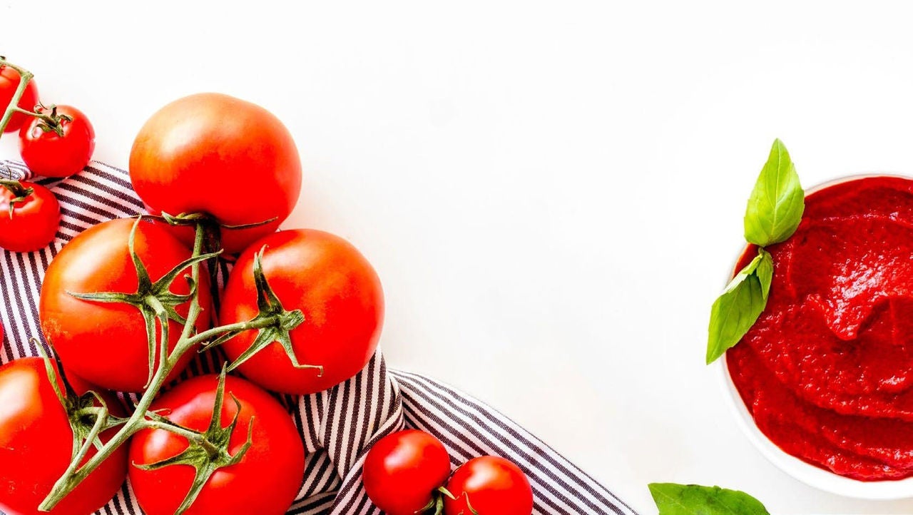  Assorted tomatoes on the vine on a black and white striped cloth next to a bowl of tomato sauce