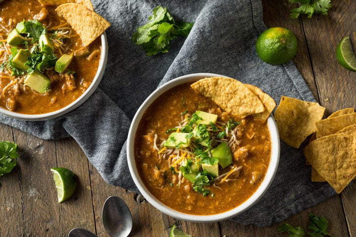 Bowl of tortilla soup with avocado pieces, cilantro and tortilla chips for garnish.