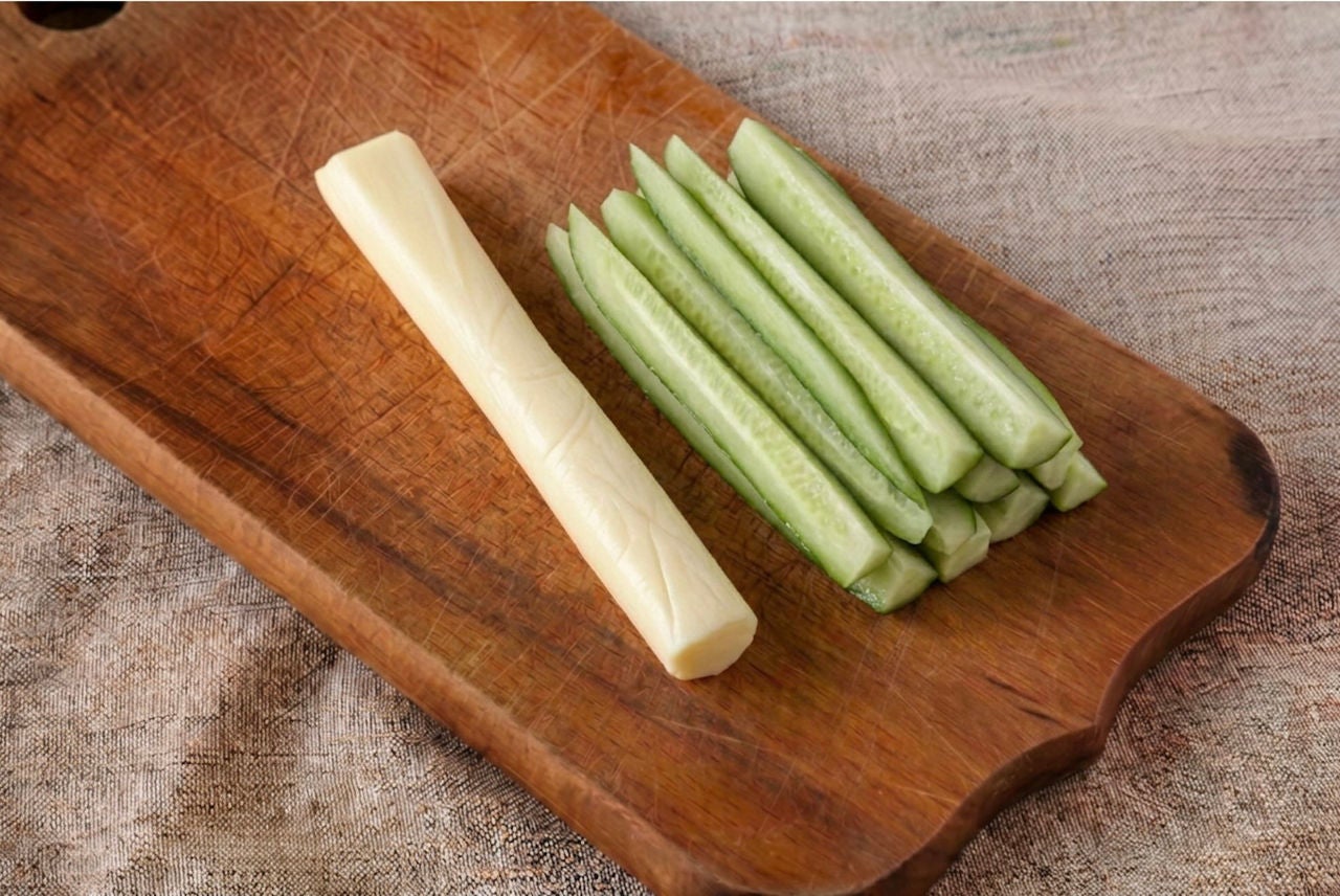 String cheese and slices of cucumber on a wooden cutting board.