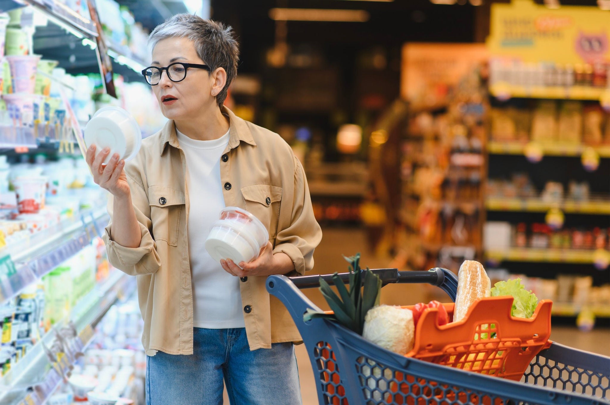 Woman reading nutrition label on product in grocery store aisle.