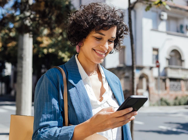 Woman outdoors looking at her phone while managing healthcare on the go.