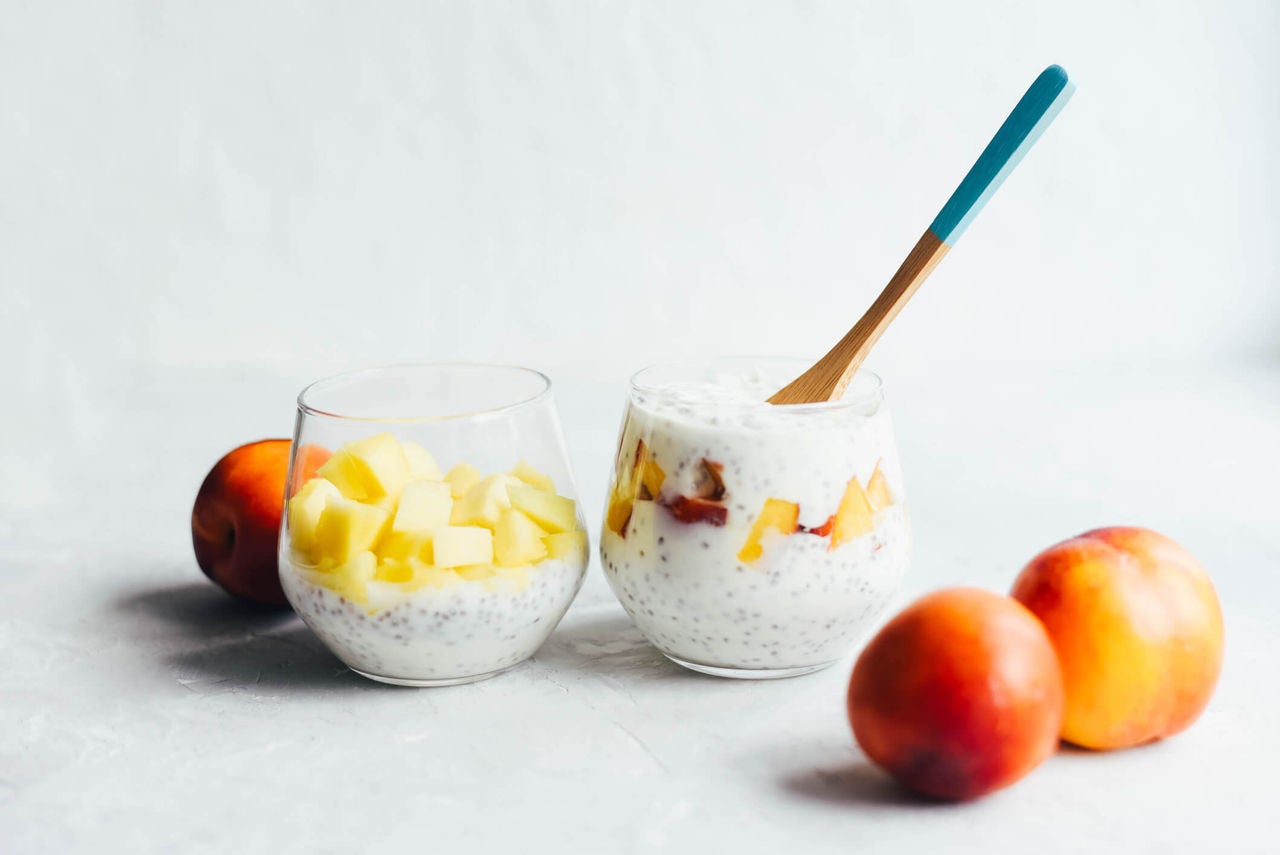 Cups with yogurt, flax seeds and pieces of apricots next to three whole apricots.
