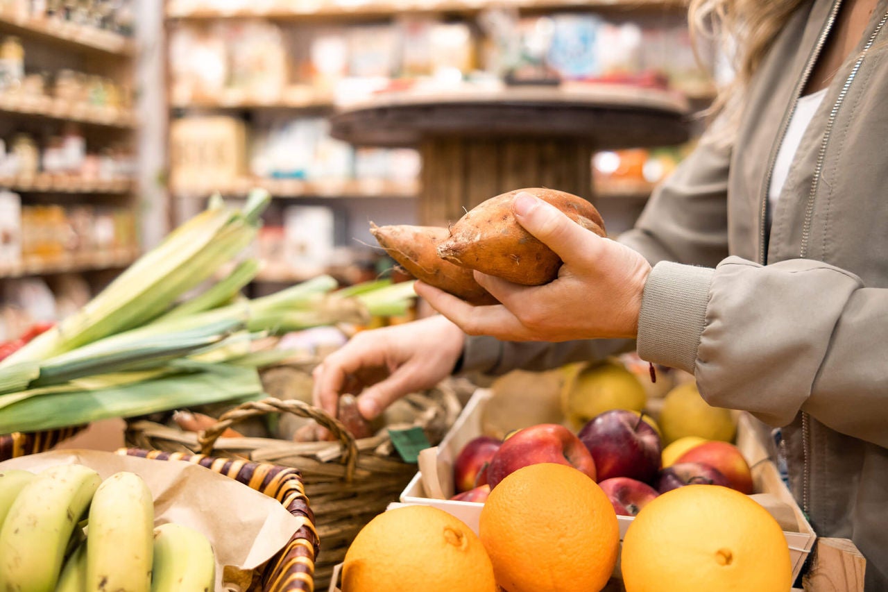 Woman picking up two sweet potatoes from a grocery store produce section. 