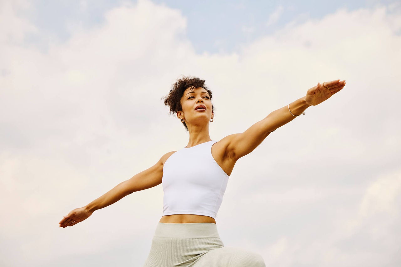 Woman performing warrior pose with blue sky in the background.