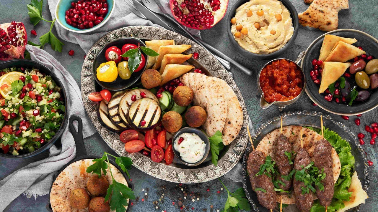 Spread of mediterranean food on a table garnished with leaves, dried peppers and pomegranate seeds.