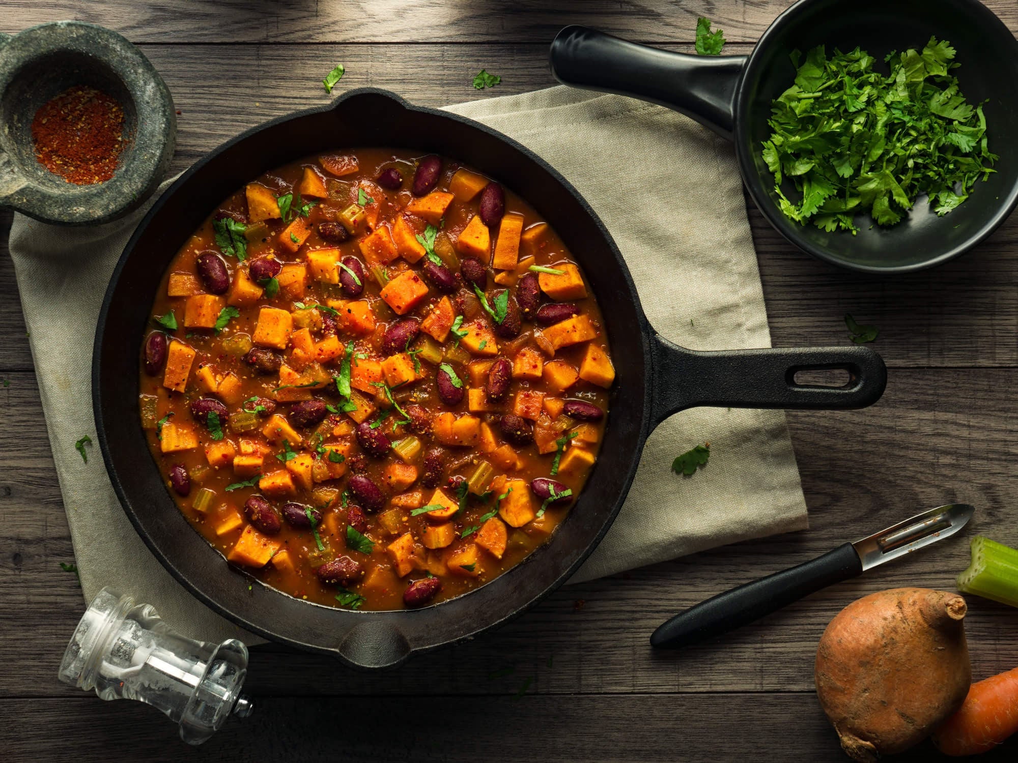 Skillet with black beans and sweet potato pieces with cilantro and spices on the side.