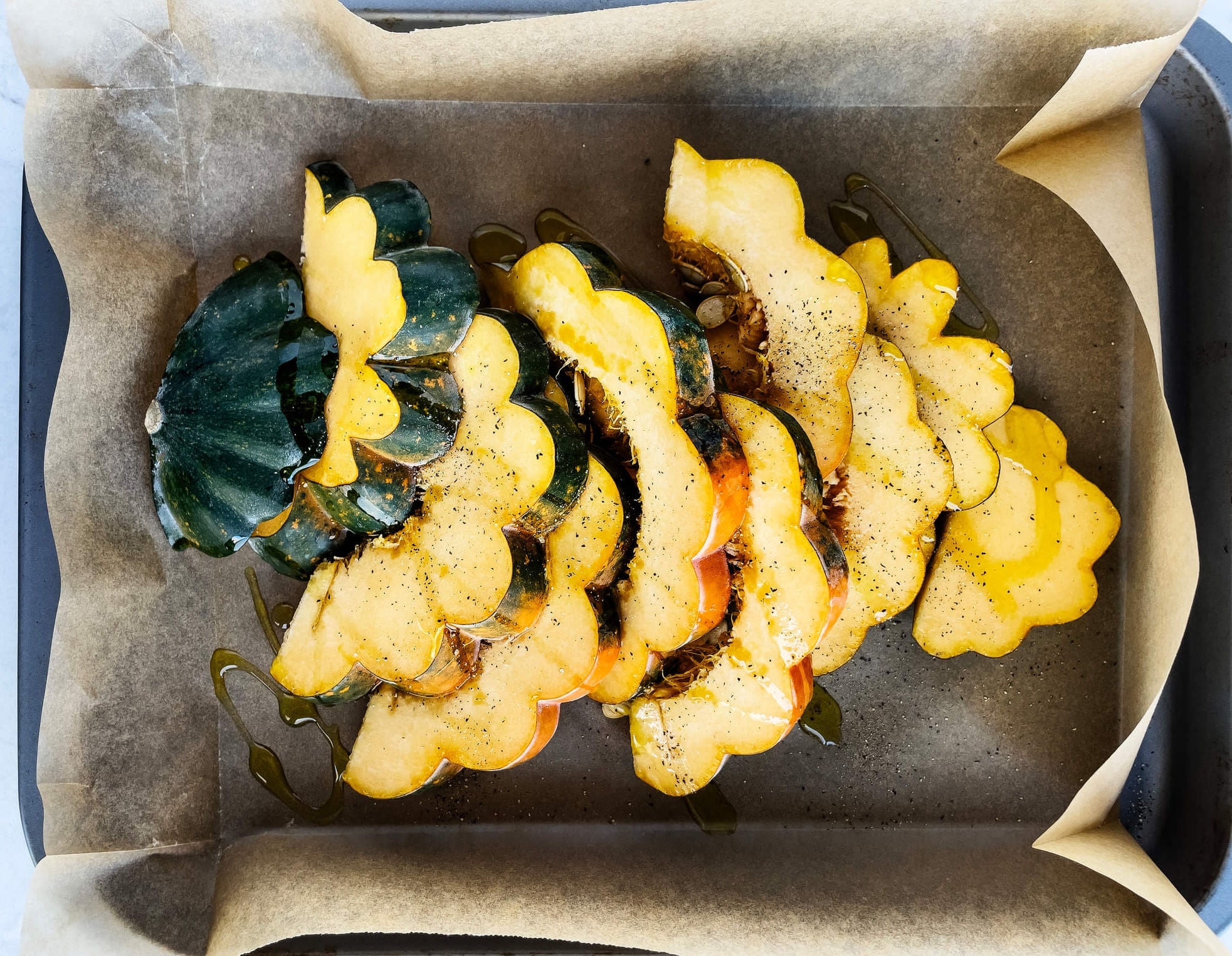 Acorn squash wedges on a pan drizzled in maple syrup.