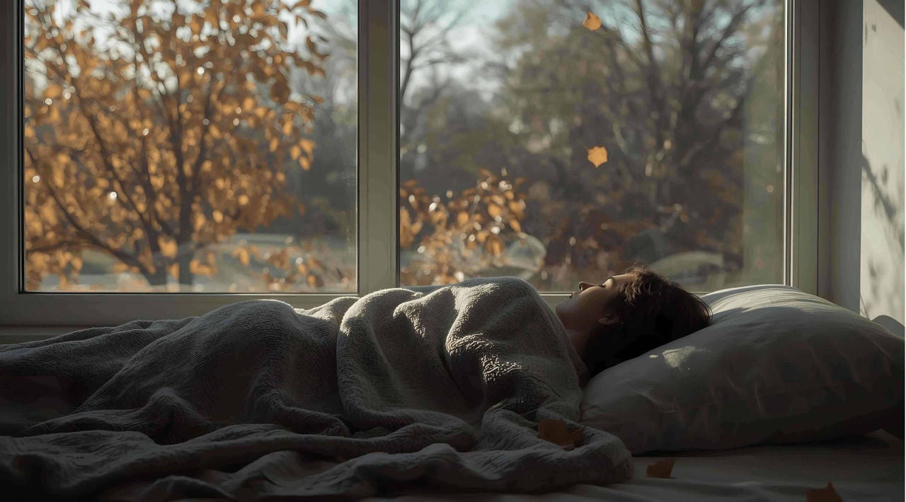 Woman peacefully sleeping in a bed by a window with autumnal scenery in the background. 