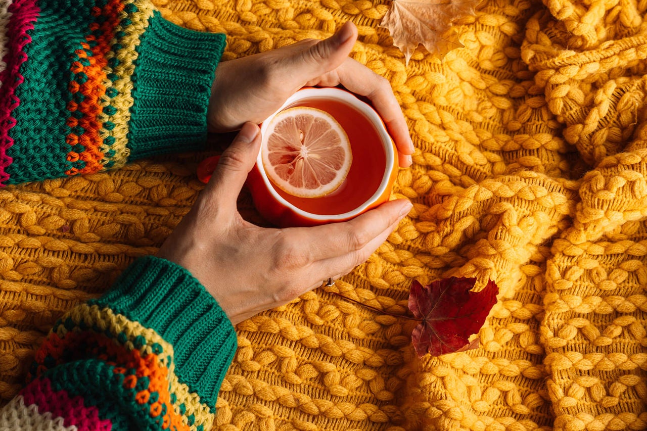 A person's hands holding a drink with a yellow blanket in the background.