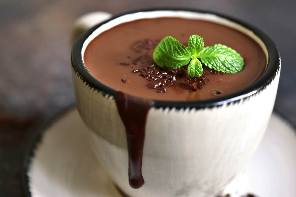 Portion of homemade mint hot chocolate in a cup on a dark slate,stone or metal background.