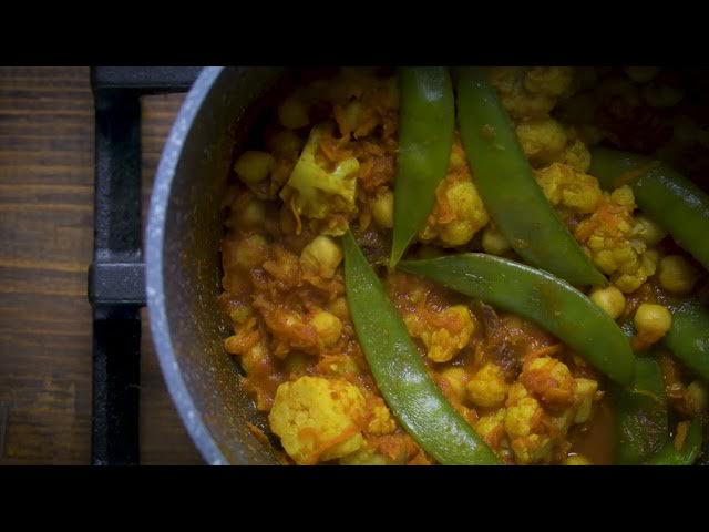 Close-up of a pot filled with a vegetable curry made of cauliflower, chickpeas, and snap peas in a rich tomato-based sauce