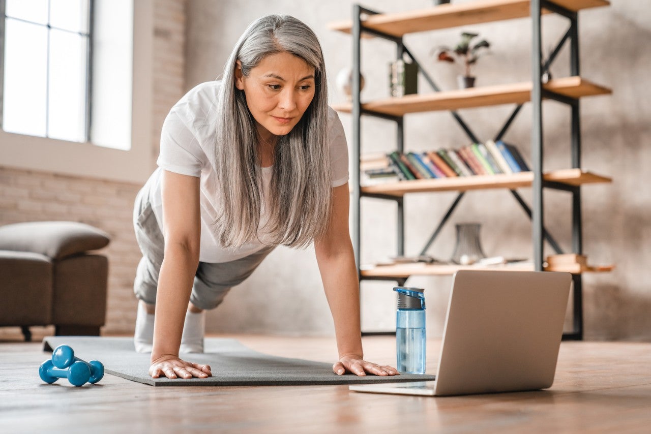 Woman doing a plank exercise while following a workout video on her laptop.