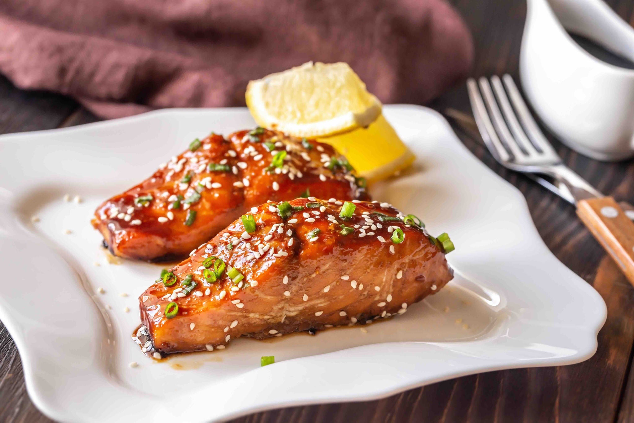 Plate with two glazed salmon fillets topped with sesame seeds and green onions.
