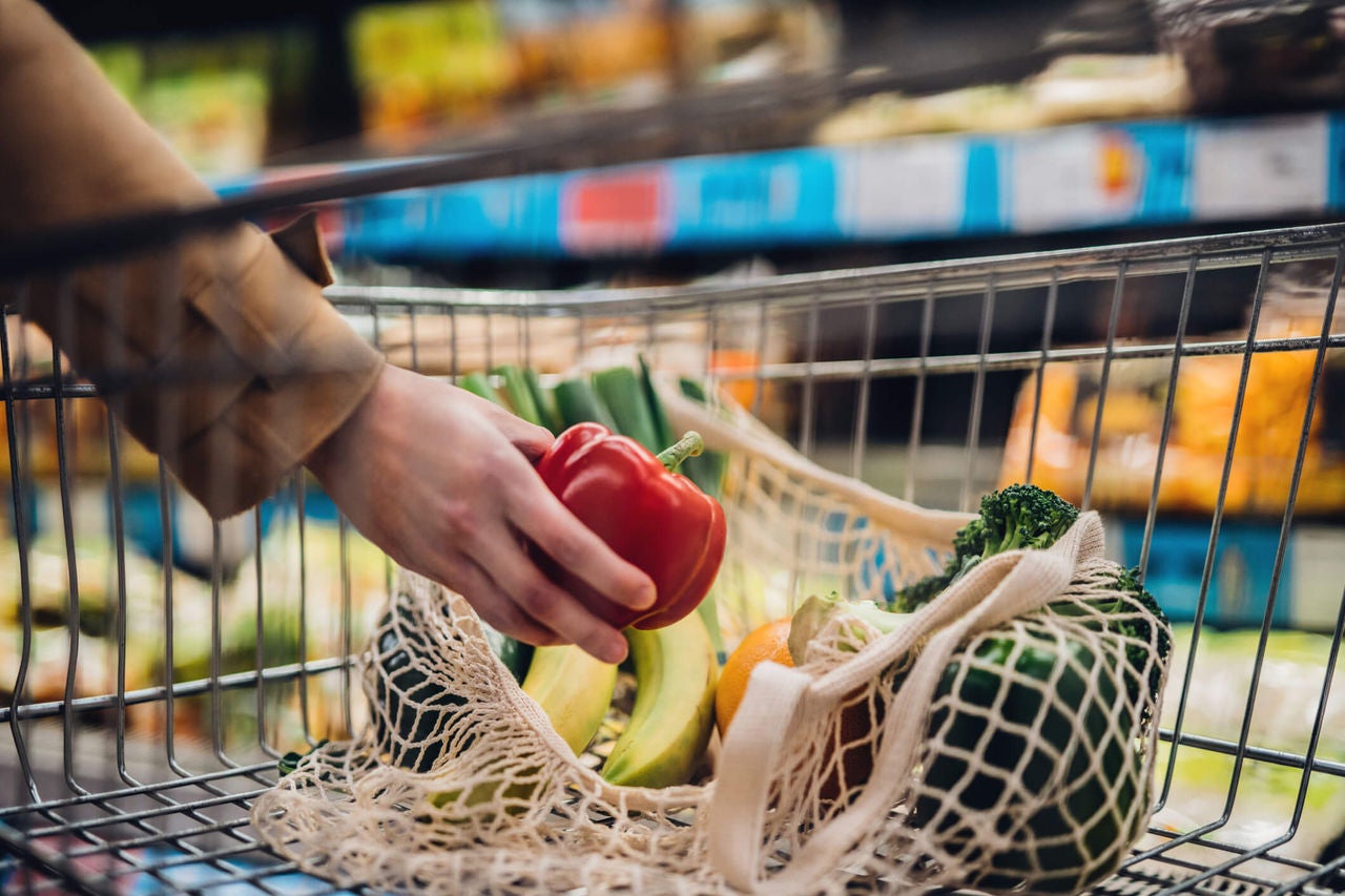 Hand reaching to put a red bell pepper into a mesh bag inside of a shopping cart