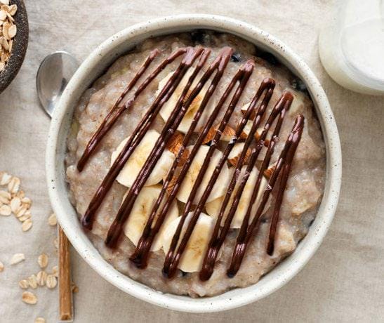 Oatmeal in a white bowl with banana slices and chocolate drizzle on top