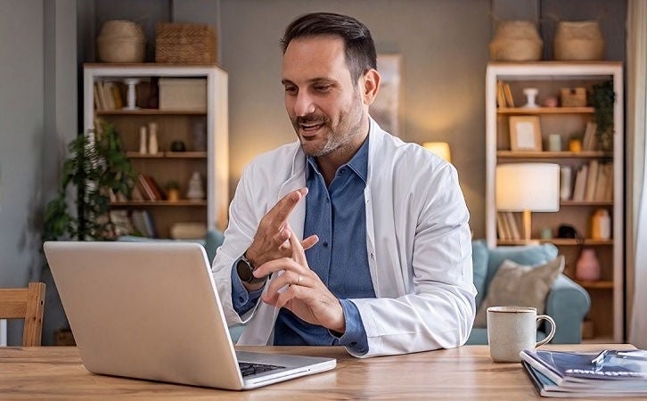 Healthcare professional using a laptop during a video consultation from a home office.