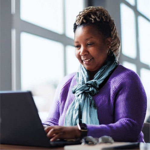 A smiling woman in a professional setting sits at a desk with a tablet.