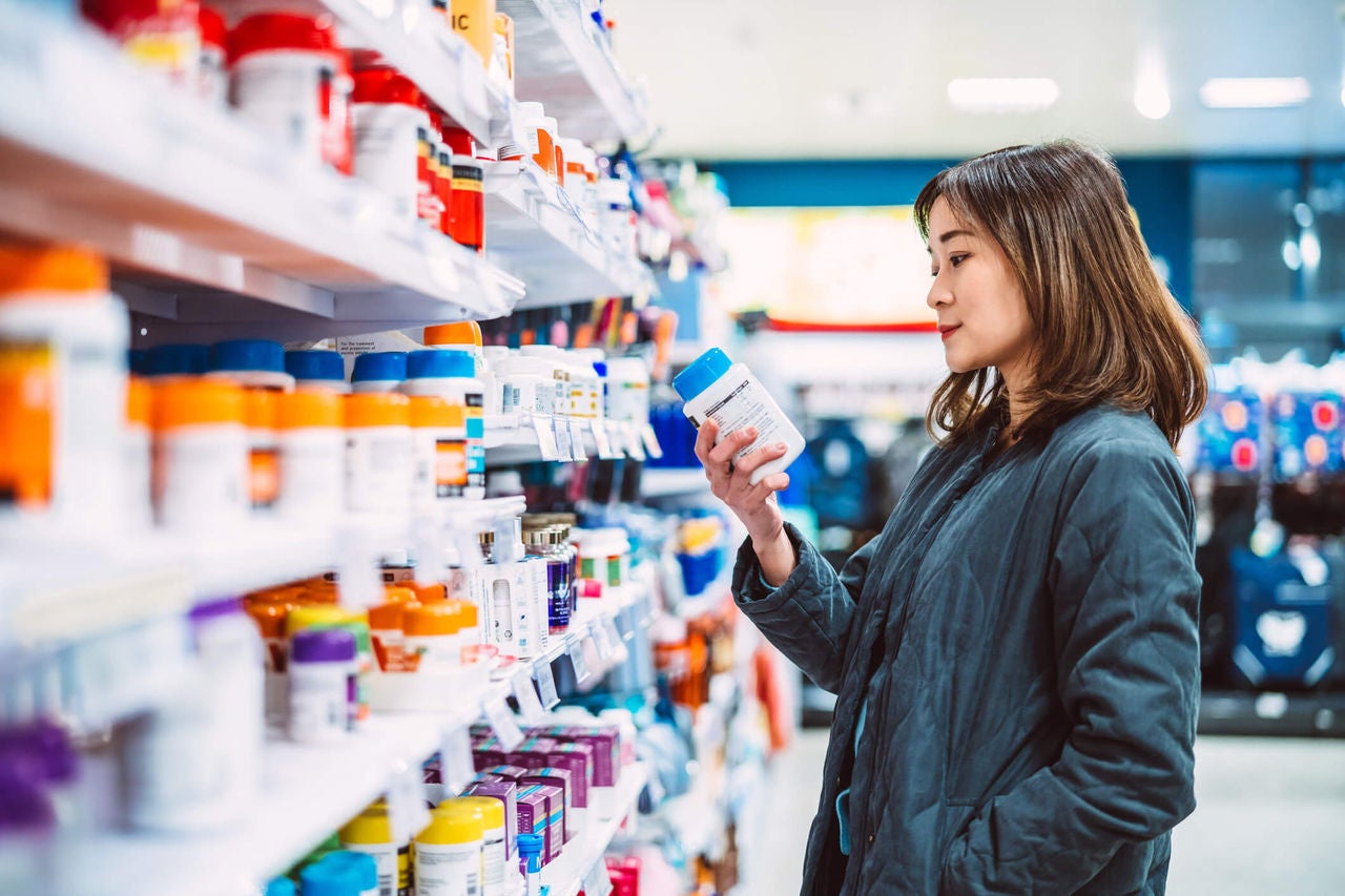 Woman looking at a bottle of nutrition supplements in a grocery store aisle.