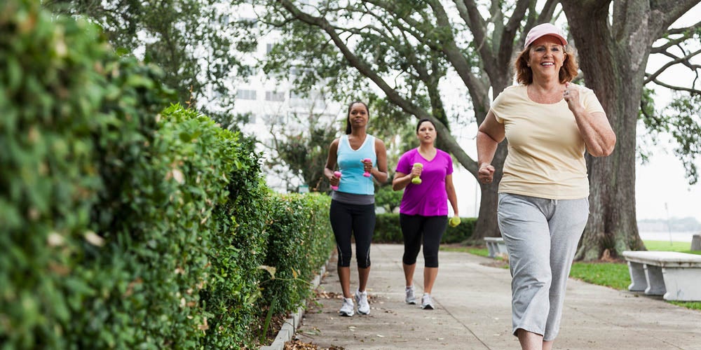 Mujeres mayores caminando y trotando al aire libre en un sendero rodeado de árboles