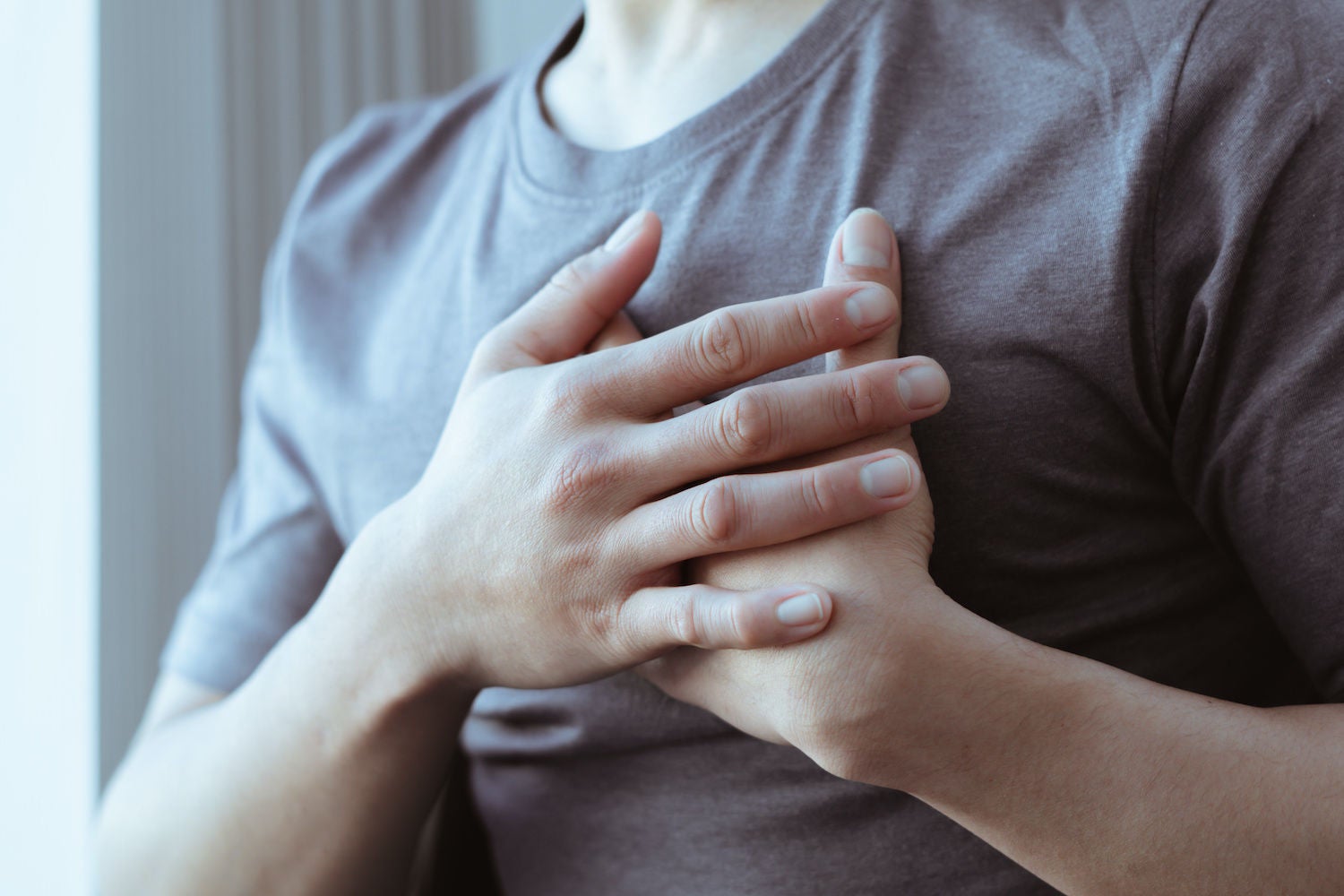 Person in a gray shirt with both hands over their heart. 