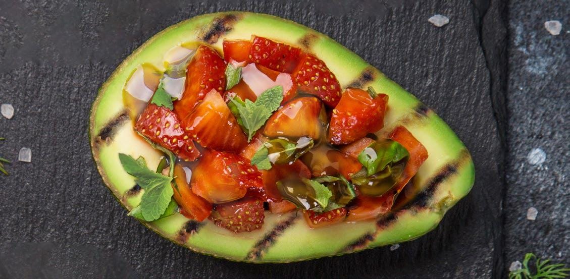 Grilled avocado with strawberry and honey sitting on a dark counter