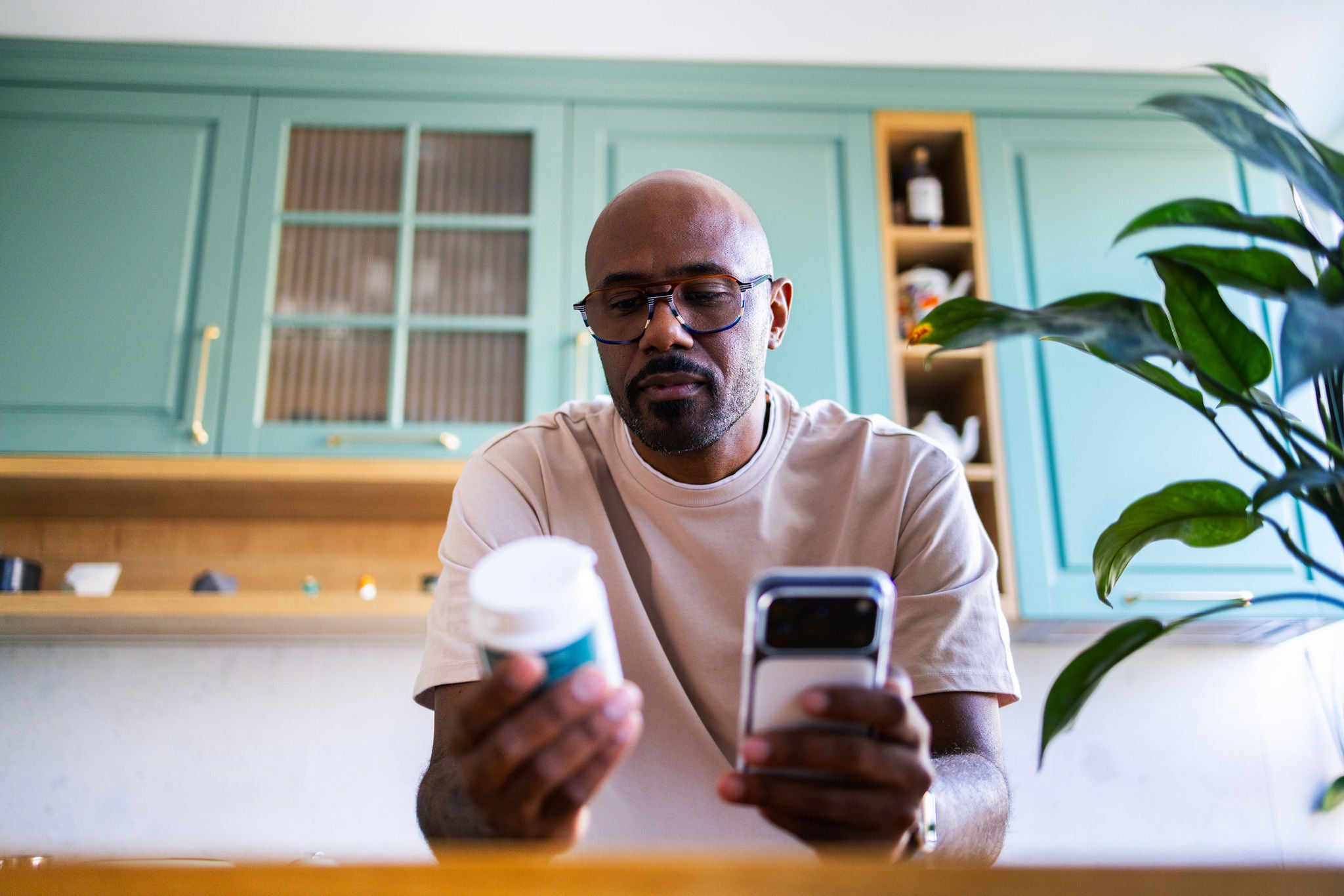 Man sitting at a table, looking at a bottle of supplements and a cell phone.
