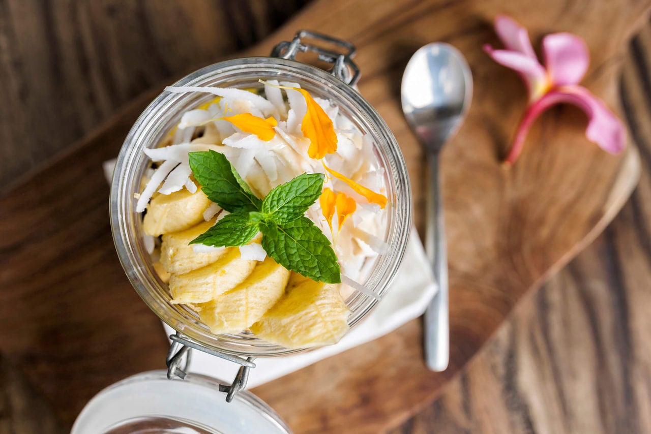 Jar with yogurt, sliced bananas, shredded coconut and mint.