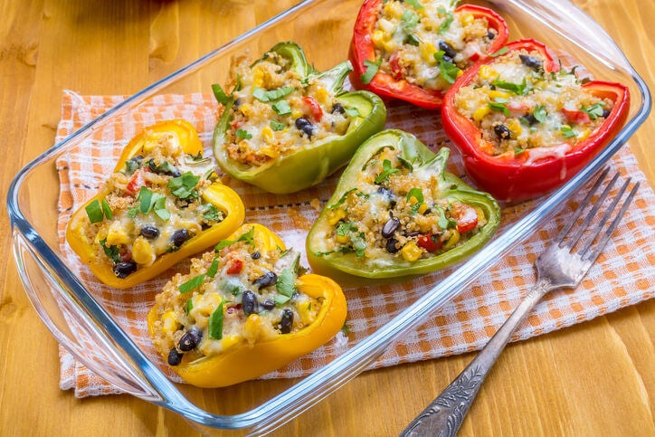 Red, green and yellow peppers stuffed with quinoa and black beans in a glass baking dish