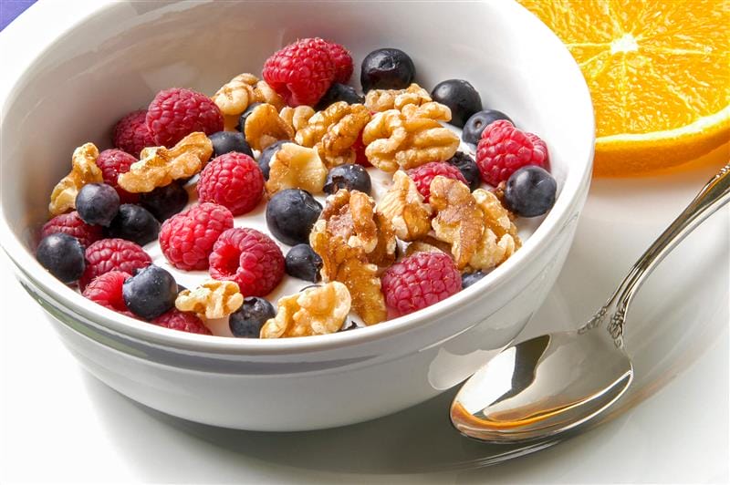 Bowl of yogurt topped with raspberries, blueberries, and walnuts