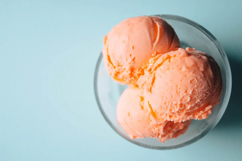 Bowl of strawberry ice cream scoops on a blue background.