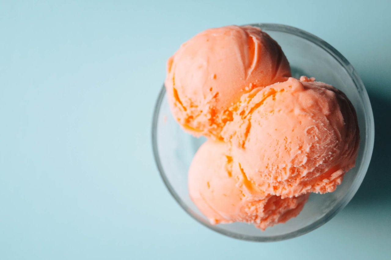 Bowl of pink ice cream scoops on a blue background.