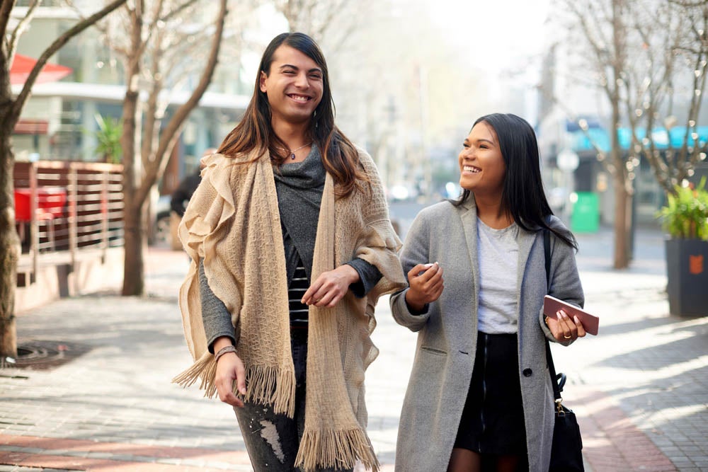 Cropped shot of two affectionate young friends having a discussion while walking in the city