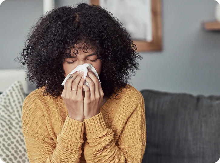  Woman sitting indoors holding a tissue while experiencing allergy or sinus symptoms.