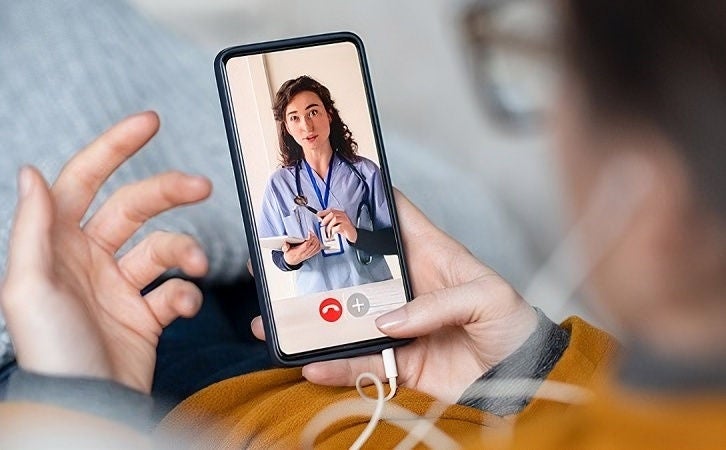 Person holding a smartphone during a video call with a healthcare professional.