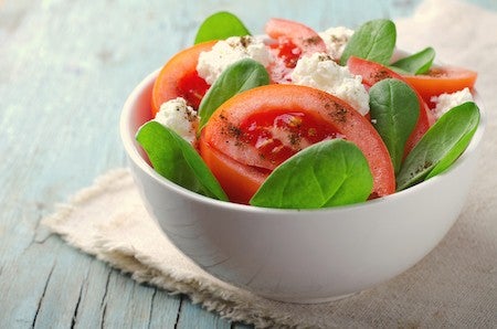 Tomato salad with spinach, cottage cheese, olive oil and pepper on blue wooden background, toned