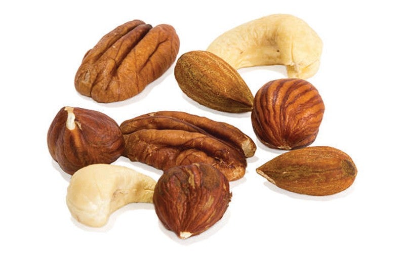 A variety of mixed nuts including pecans, hazelnuts, almonds, and cashews spread out on a white surface.