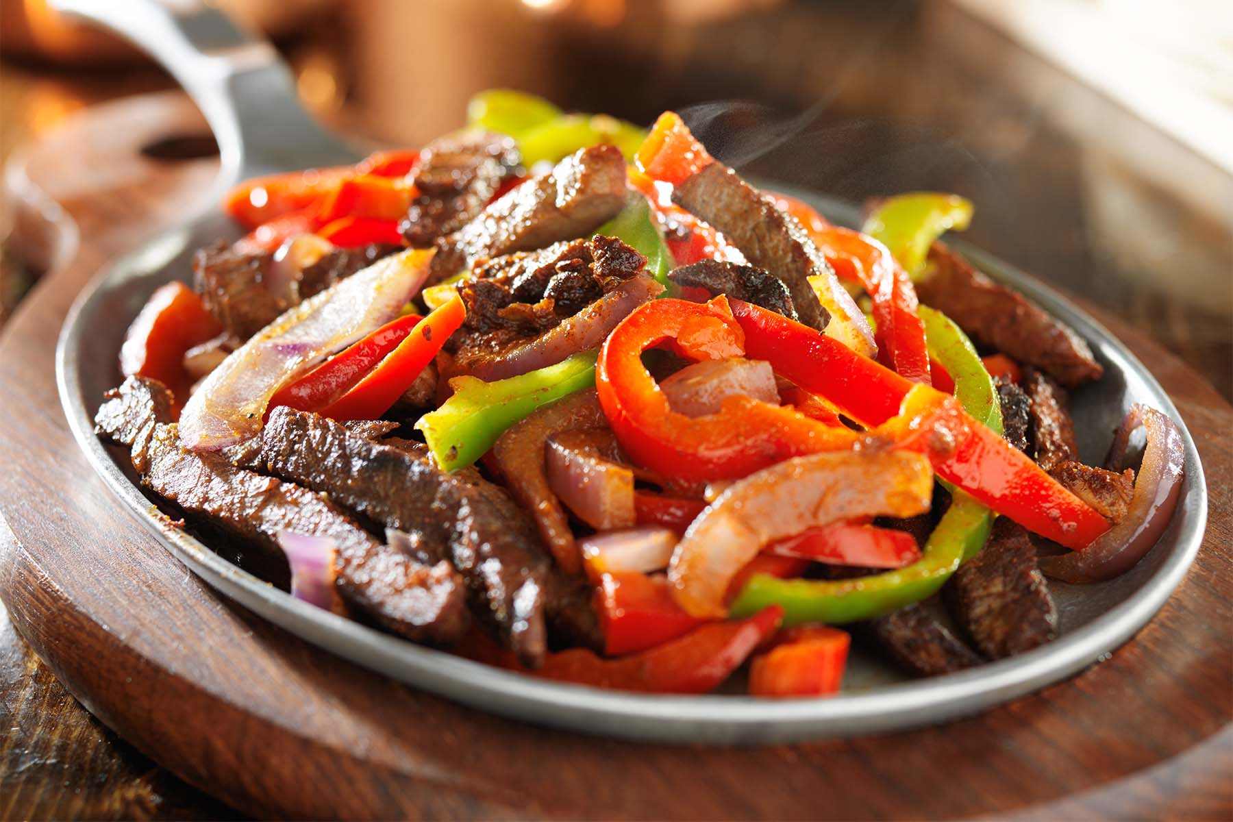 Sartén de hierro fundido con salchichas asadas, tomates cherry y diversas verduras como pimientos y calabacines, dispuesta sobre una superficie de madera