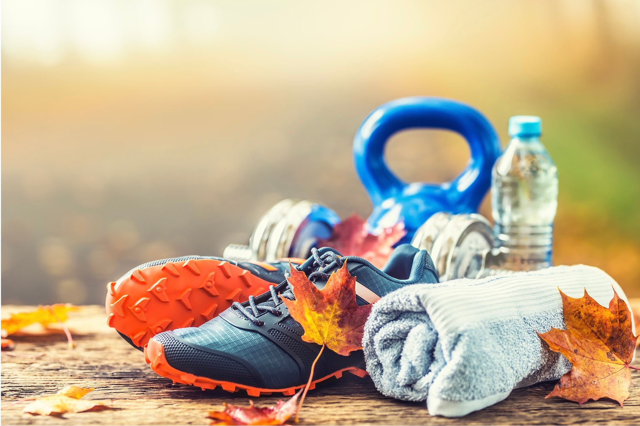Outdoor table with running shoes, dumbbells, water bottle, towel and autumn leaves.