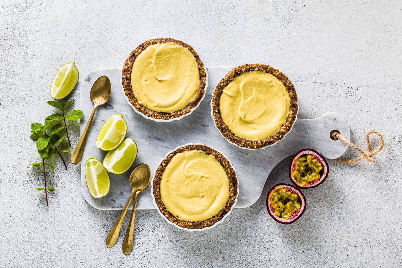 3 mini lime tarts with vegan date crusts with quartered limes and mint on the side.