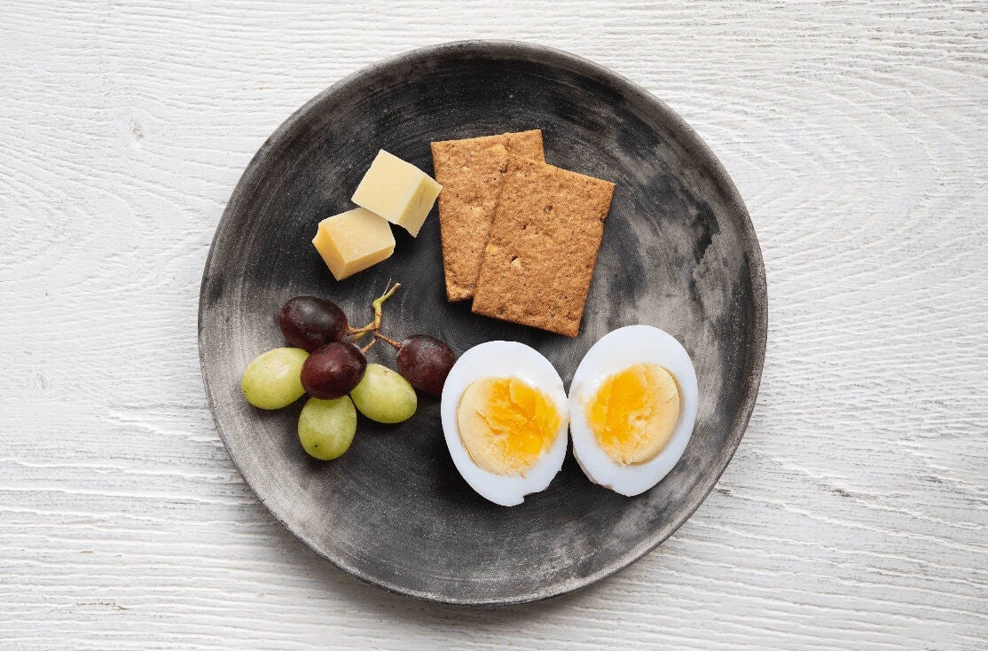 Plate with cubes of cheese, whole grain crackers, grapes and a hard boiled egg sliced in half.