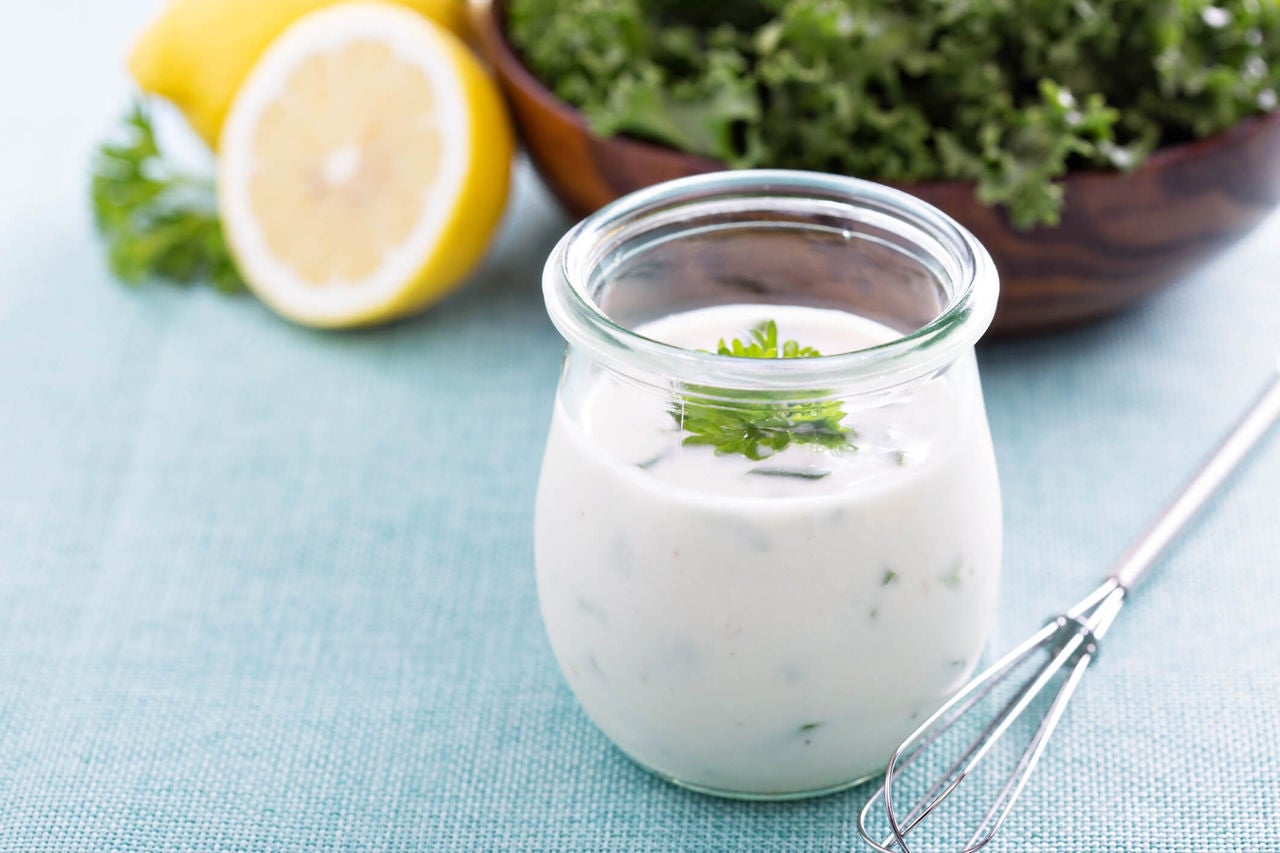 Ranch dressing in a small glass jar with a small whisk and a bowl with salad in the background.