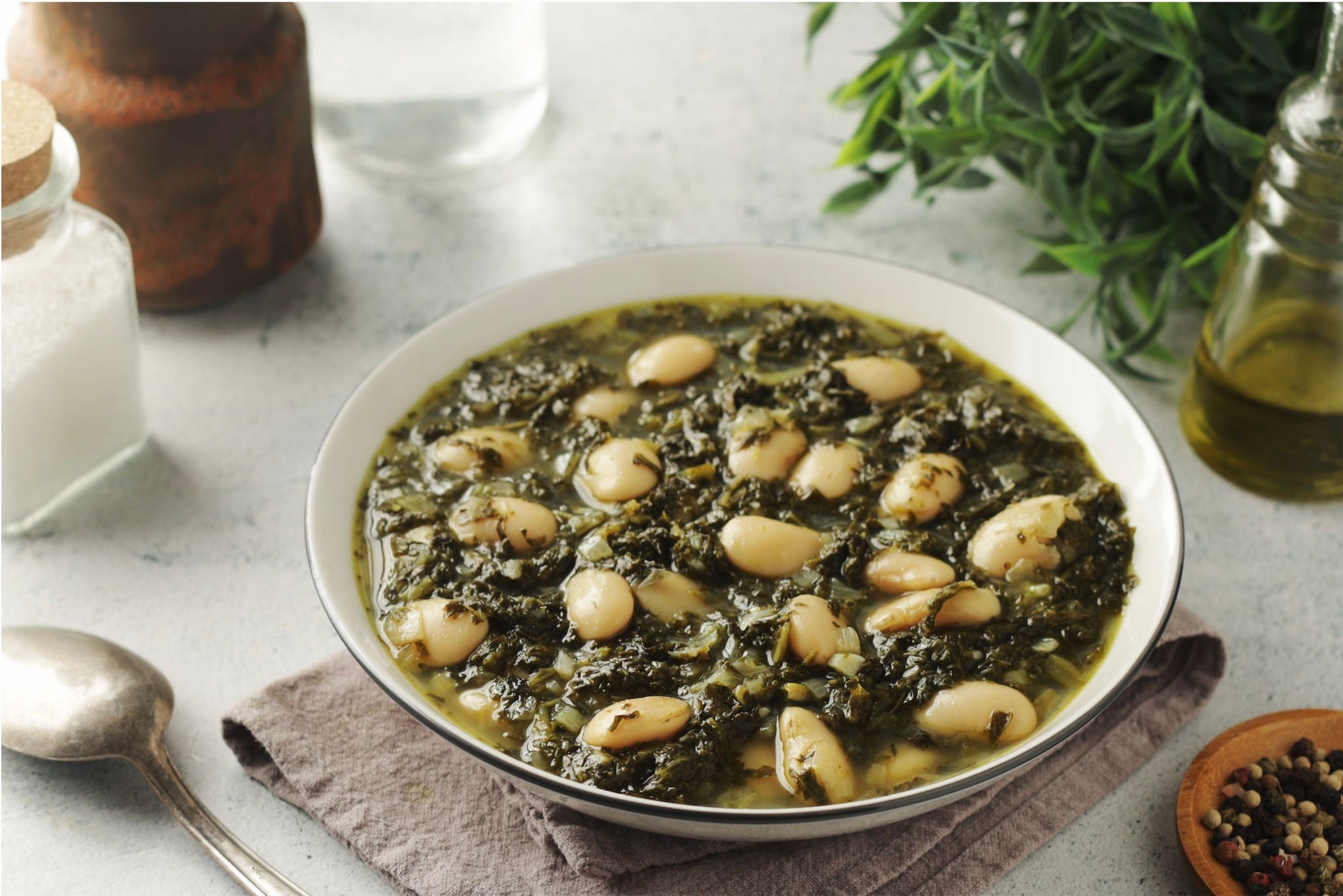 Bowl of white beans, kale and broth on a set table.