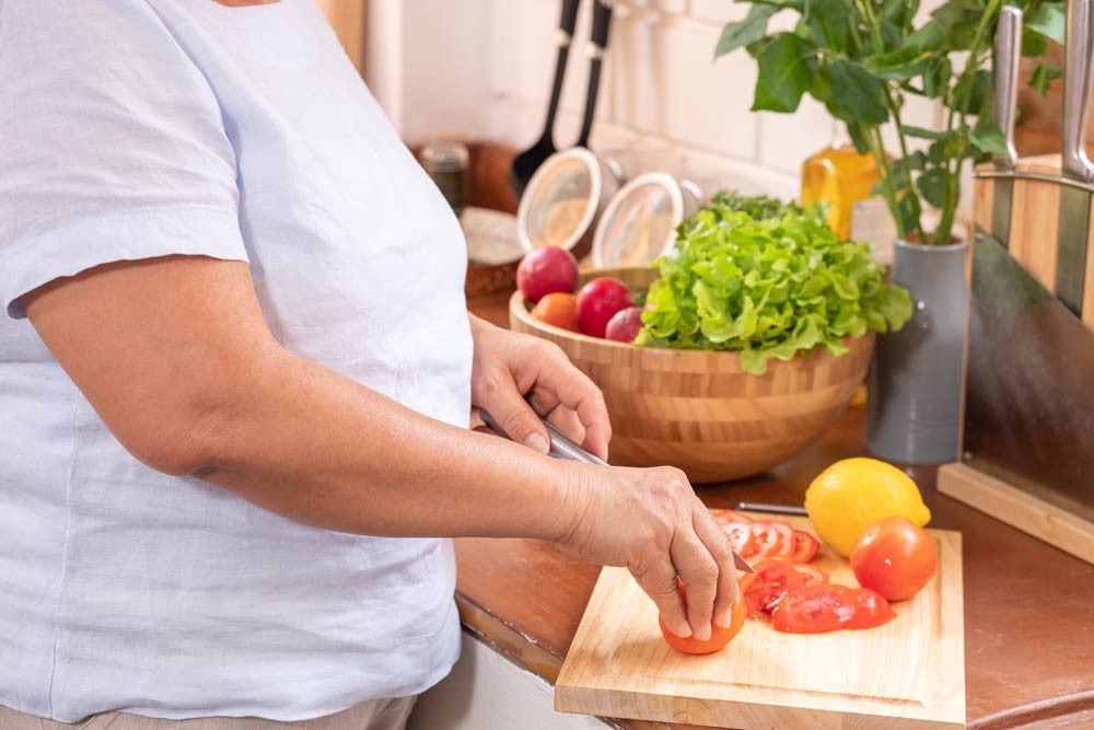 Mano de una persona mayor cortando tomates en una tabla de cortar de madera. Preparando ensalada, concepto saludable.